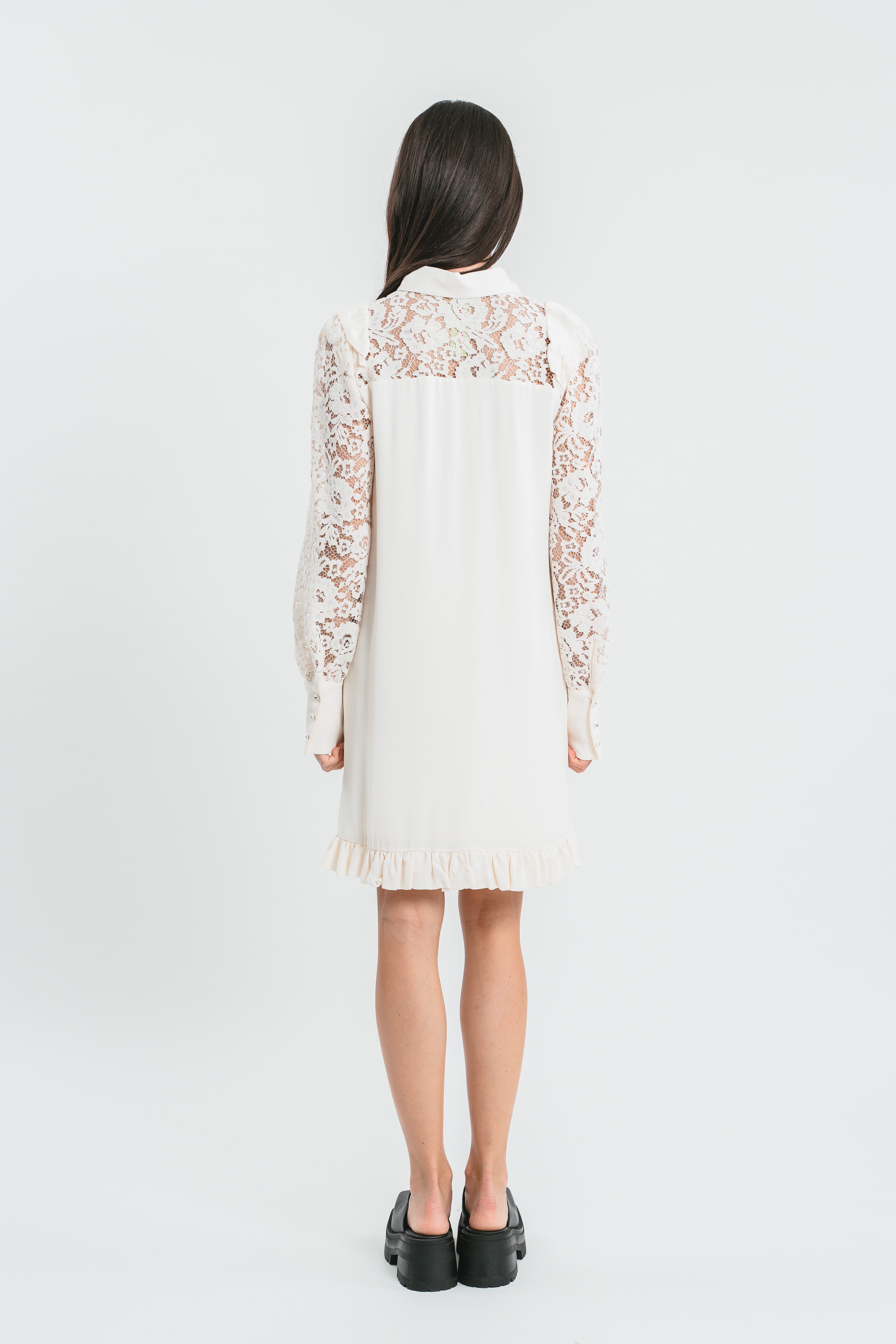 Modella indossa abito bianco corto con plastron di pizzo. Retro