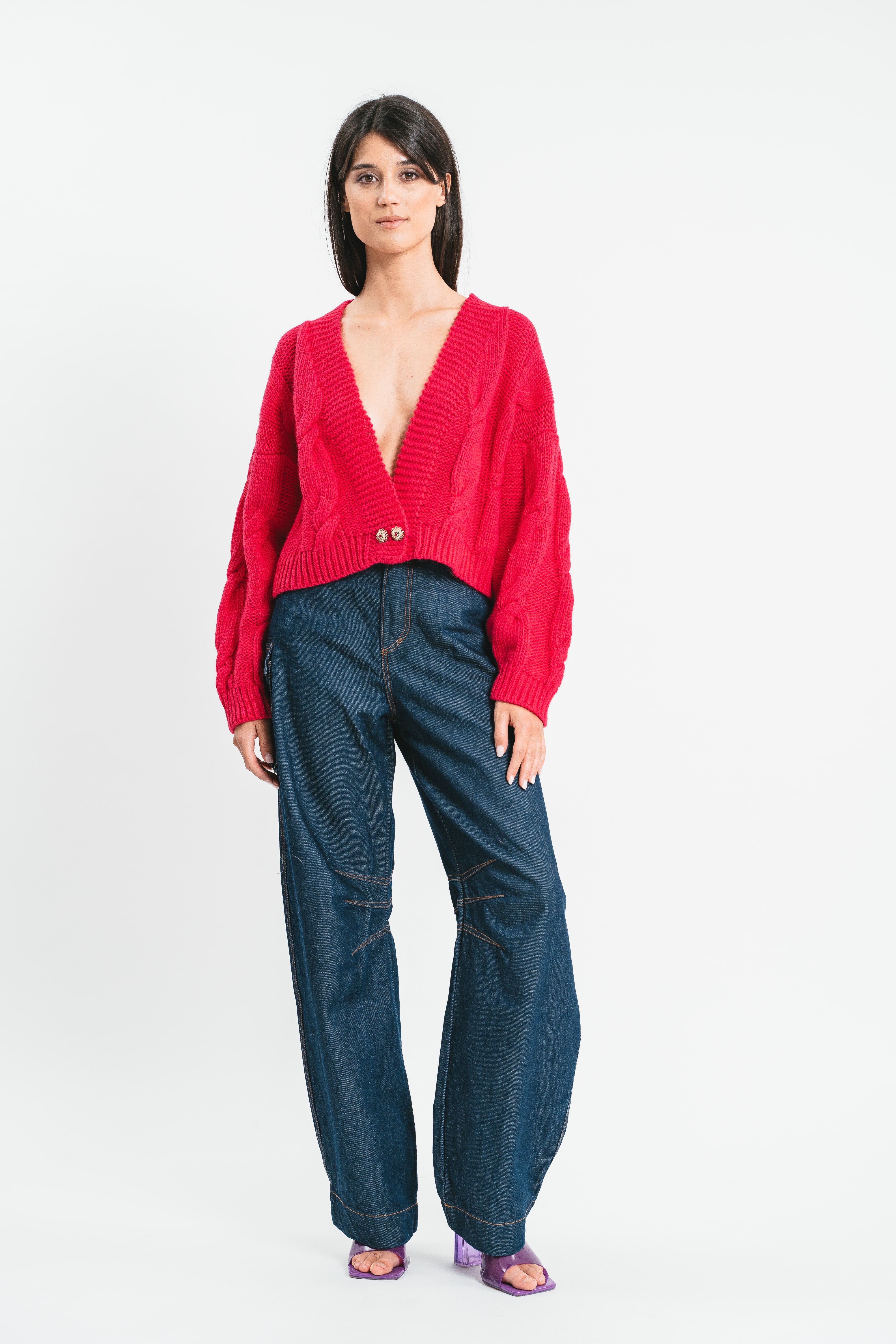 Modella indossa cardigan crop fucsia a trecce con bottone gioiello. Frontale