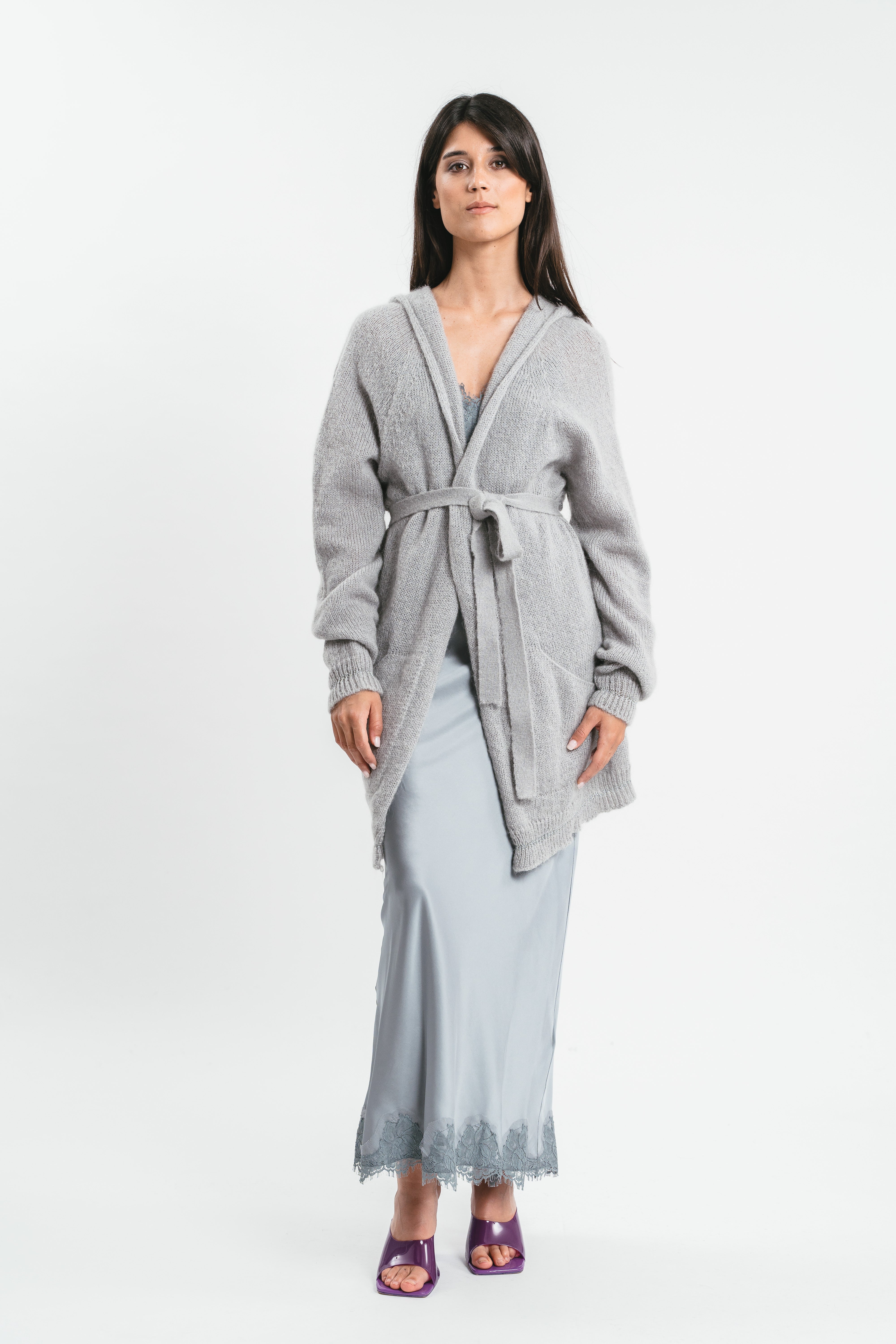 Modella indossa cardigan grigio con cappuccio e maniche arricciate con cintura in coordinato. Frontale