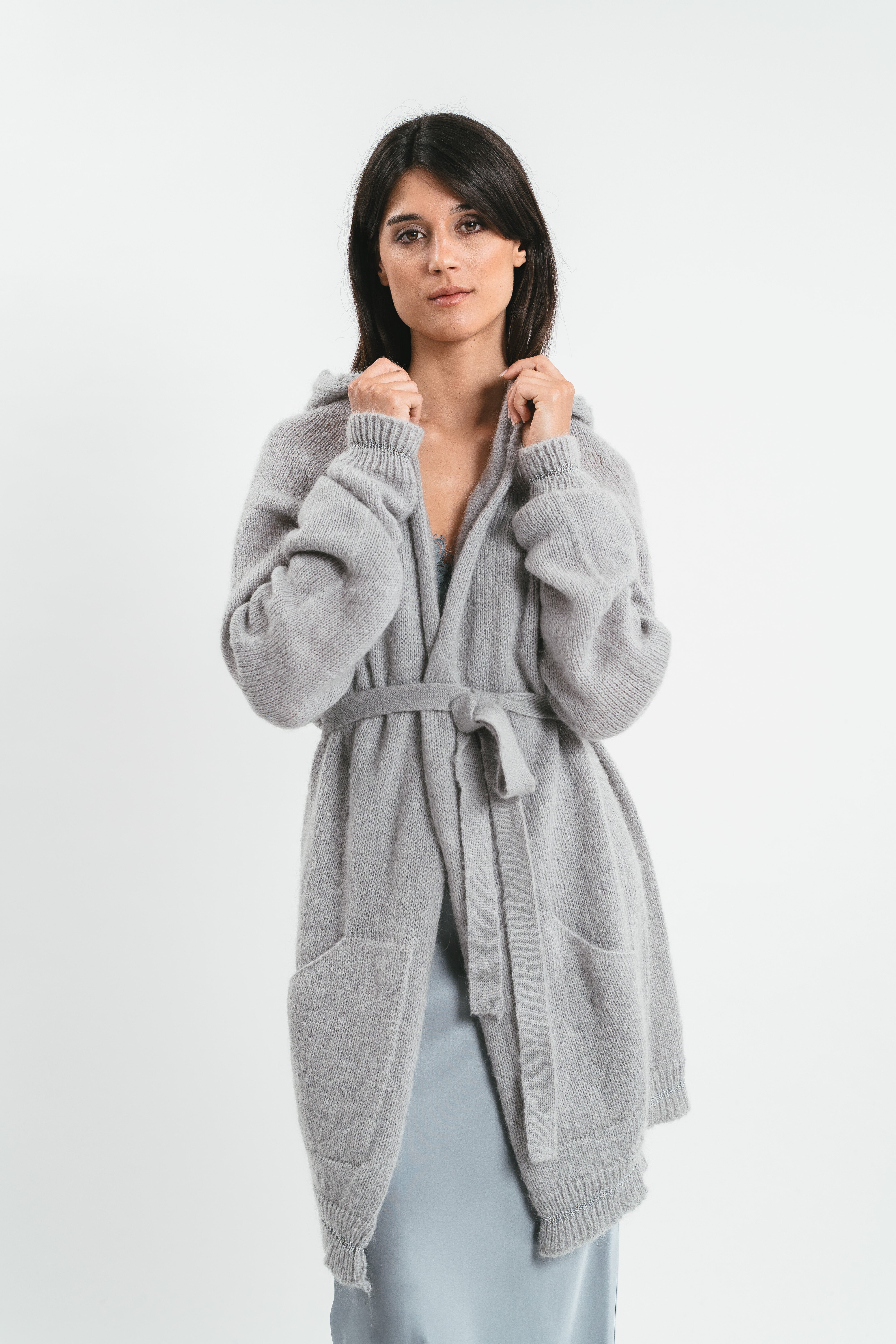 Modella indossa cardigan grigio con cappuccio e maniche arricciate con cintura in coordinato. Dettaglio
