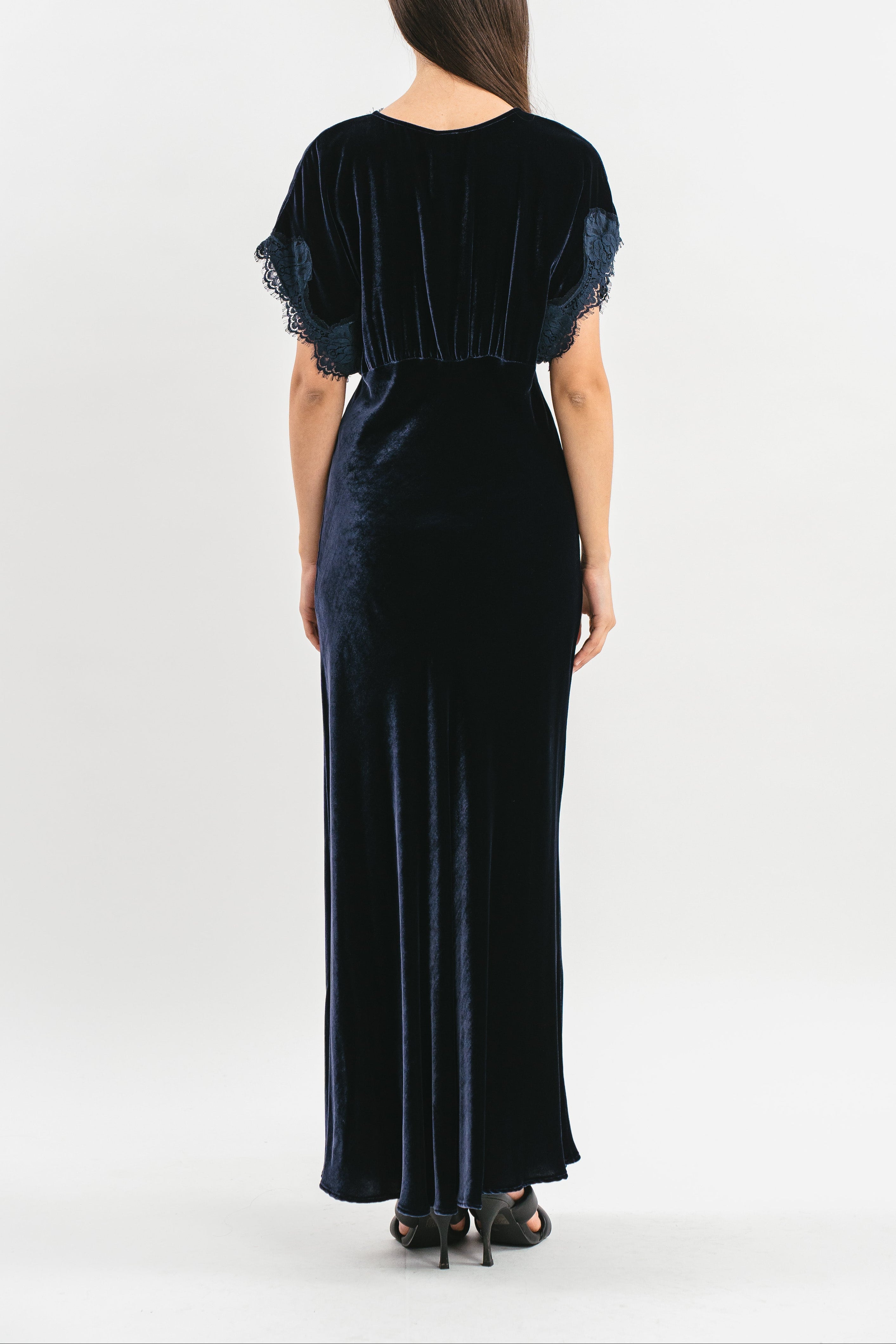 Modella indossa abito blu navy in velluto con mezze maniche e pizzo. Posteriore