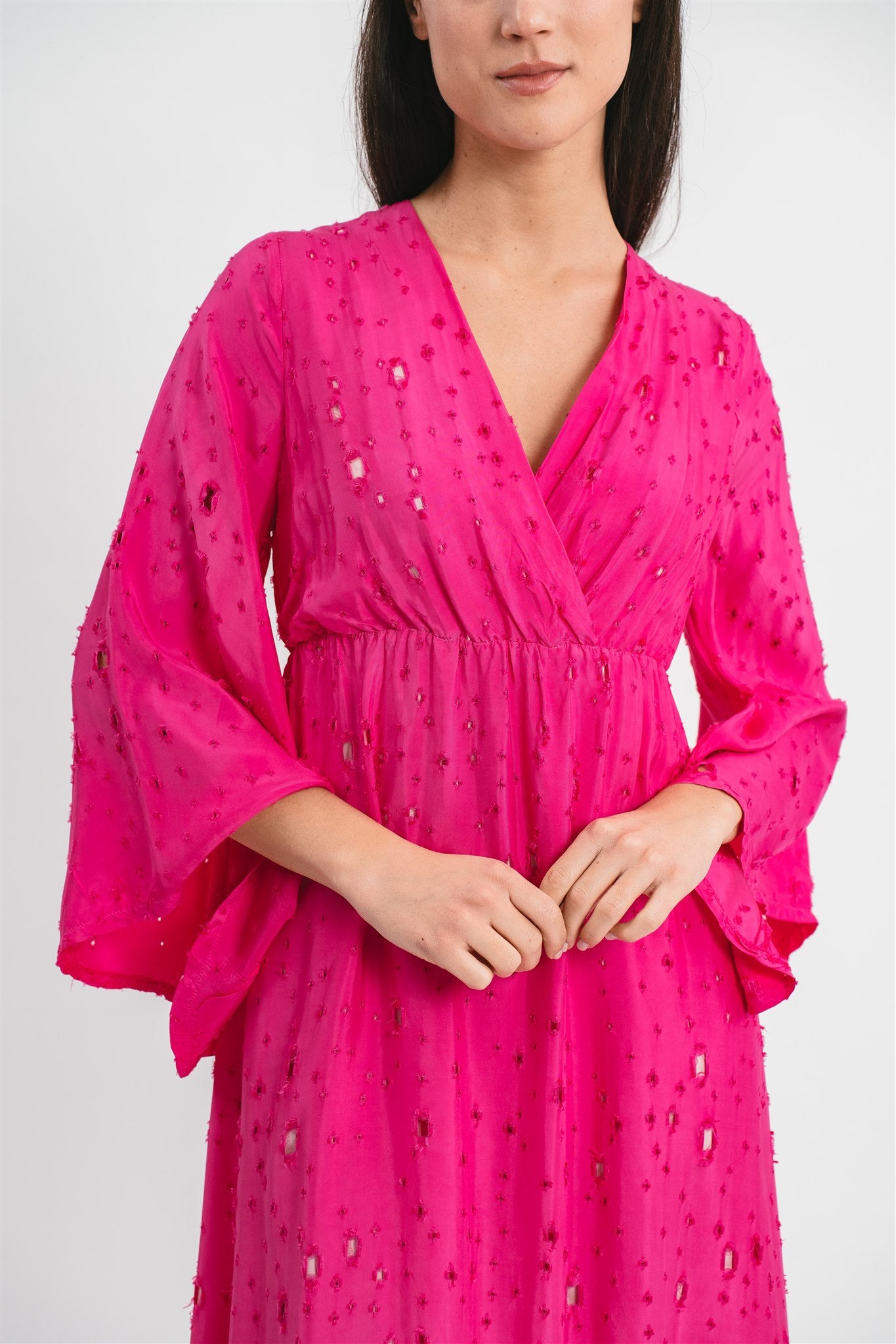 Modella indossa abito color fucsia traforato con maniche ampie. Dettaglio