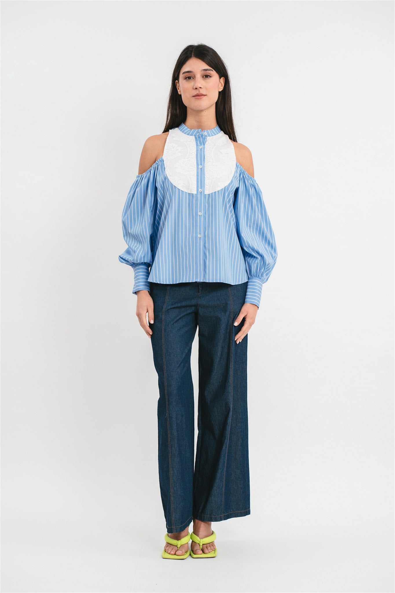 Modella indossa camicia celeste di cotone a righe con collo alla coreana e plastron in pizzo, spalle scoperte e maniche a sbuffo. Frontale