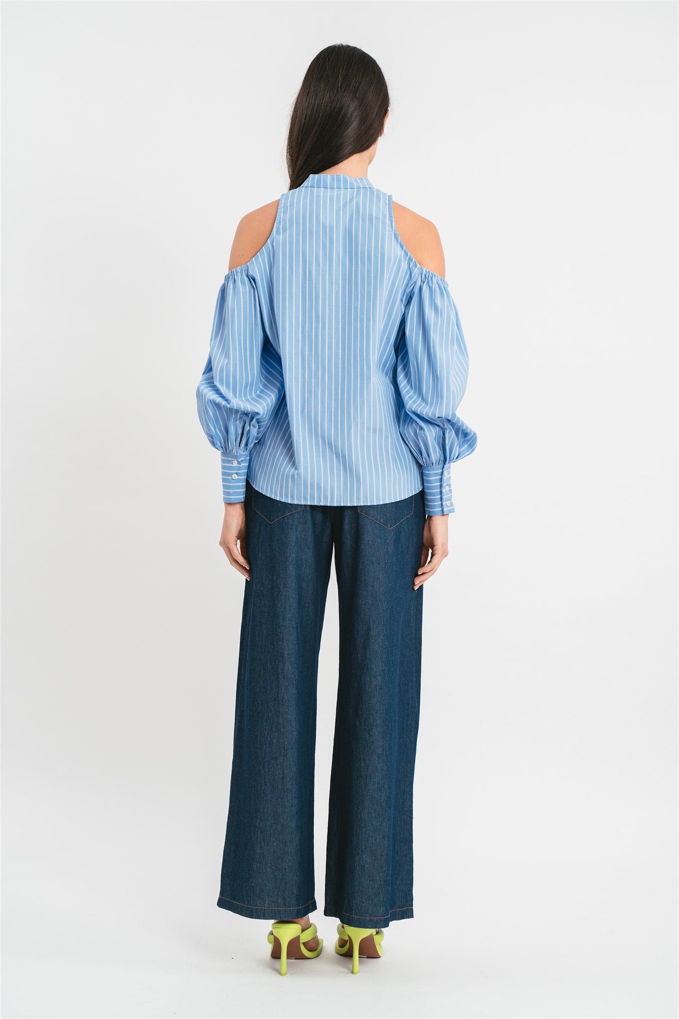 Modella indossa camicia celeste di cotone a righe con collo alla coreana e plastron in pizzo, spalle scoperte e maniche a sbuffo. Posteriore