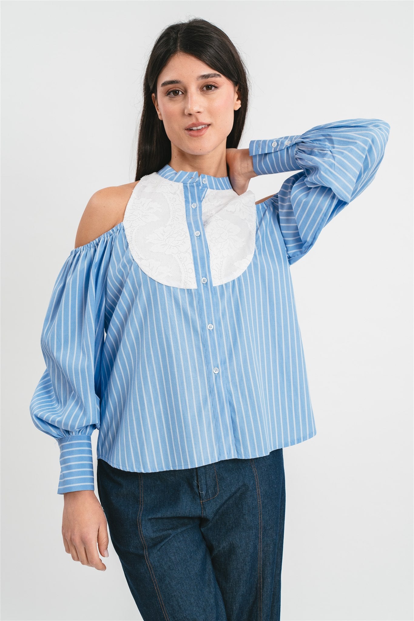 Modella indossa camicia celeste di cotone a righe con collo alla coreana e plastron in pizzo, spalle scoperte e maniche a sbuffo. Dettaglio
