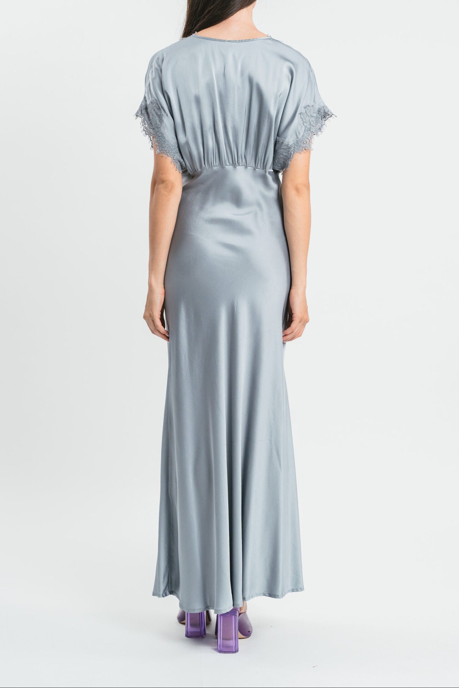 Modella indossa abito argento lungo in viscosa elasticizzata con rifiniture in pizzo francese. Retro