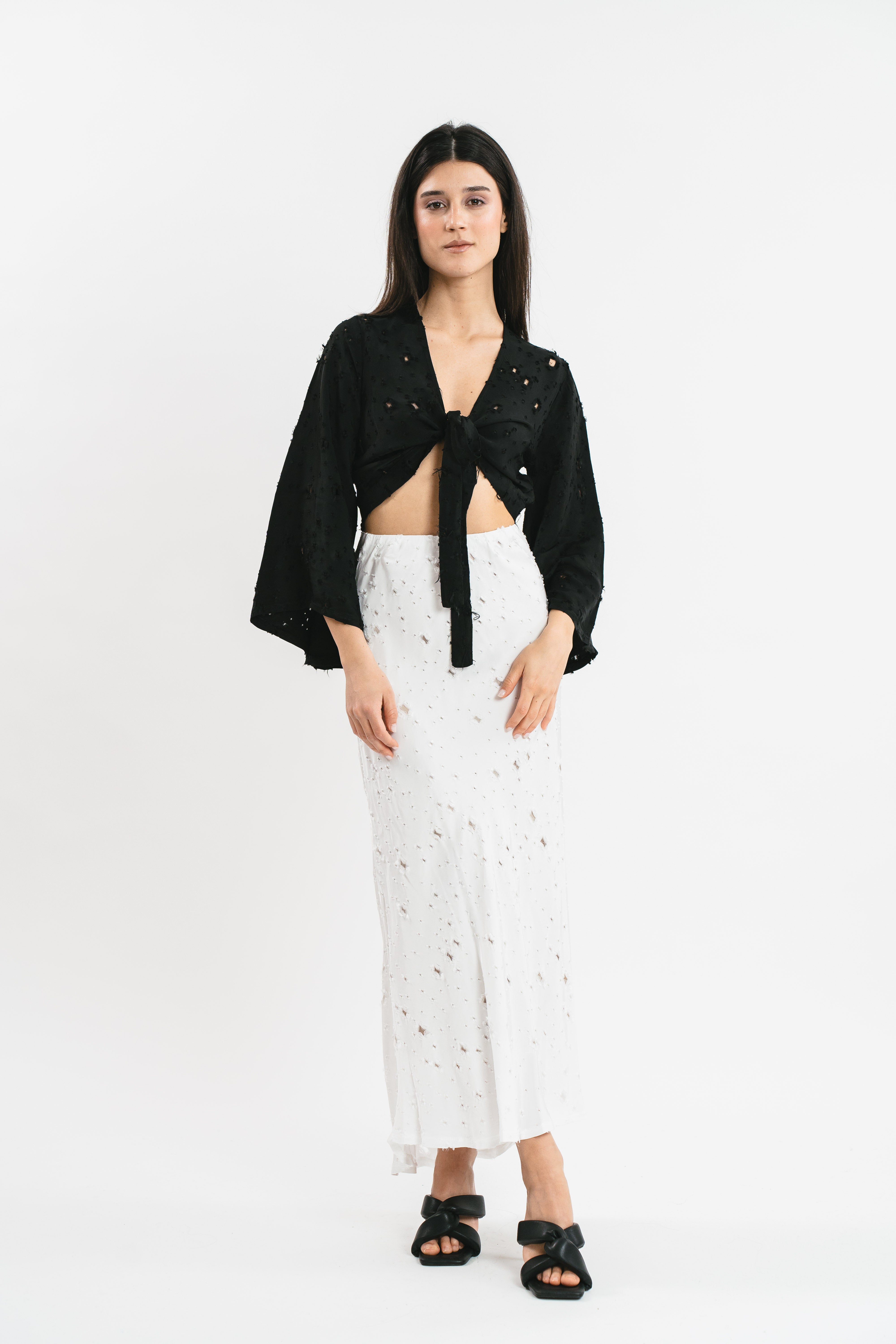 Crop top nero traforato con fiocco frontale e maniche ampie.
Frontale